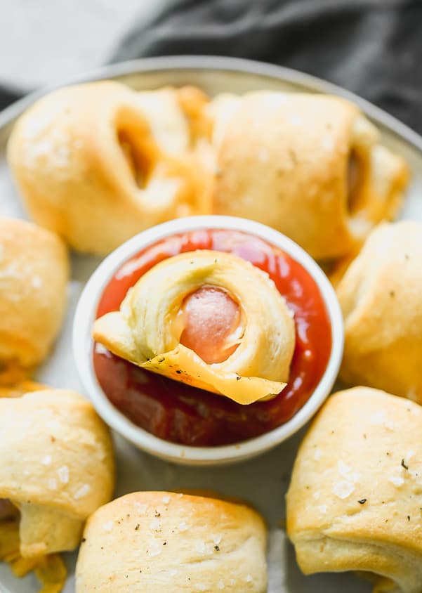 Pigs in a blanket being dipped in red marinara sauce. 