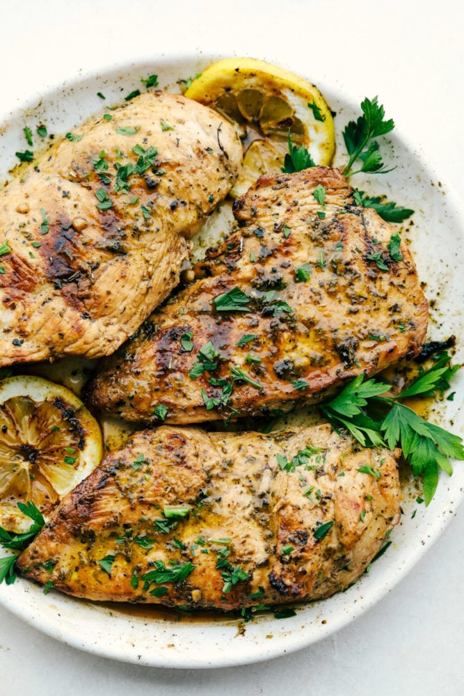 Pollo marinado cocido en un plato con guarnición verde.