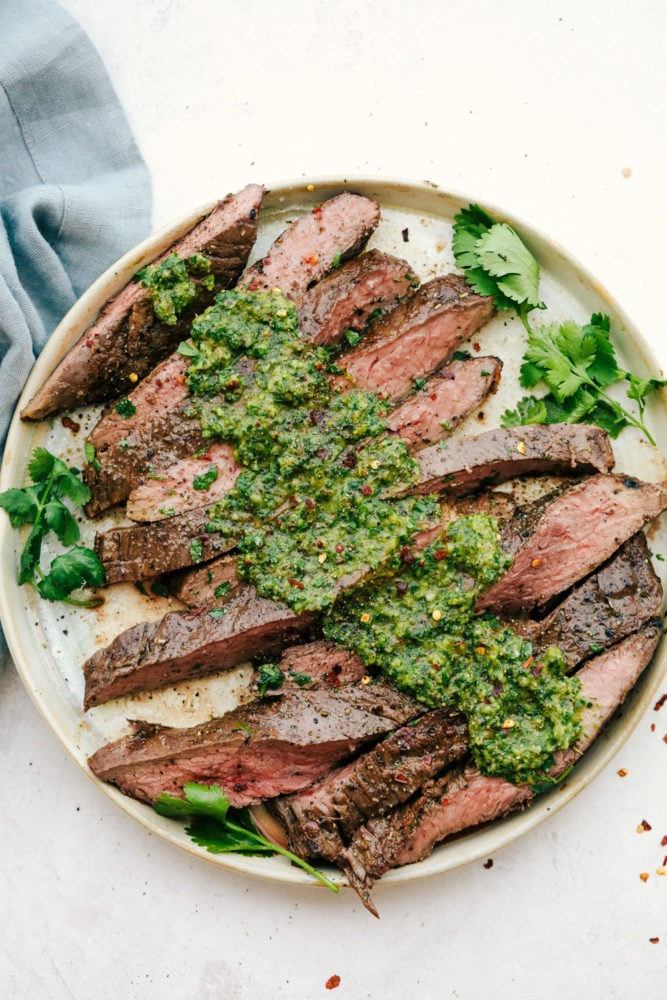 Filete de flanco rebanado contra el grano con salsa de chimichurri encima en un plato blanco. 