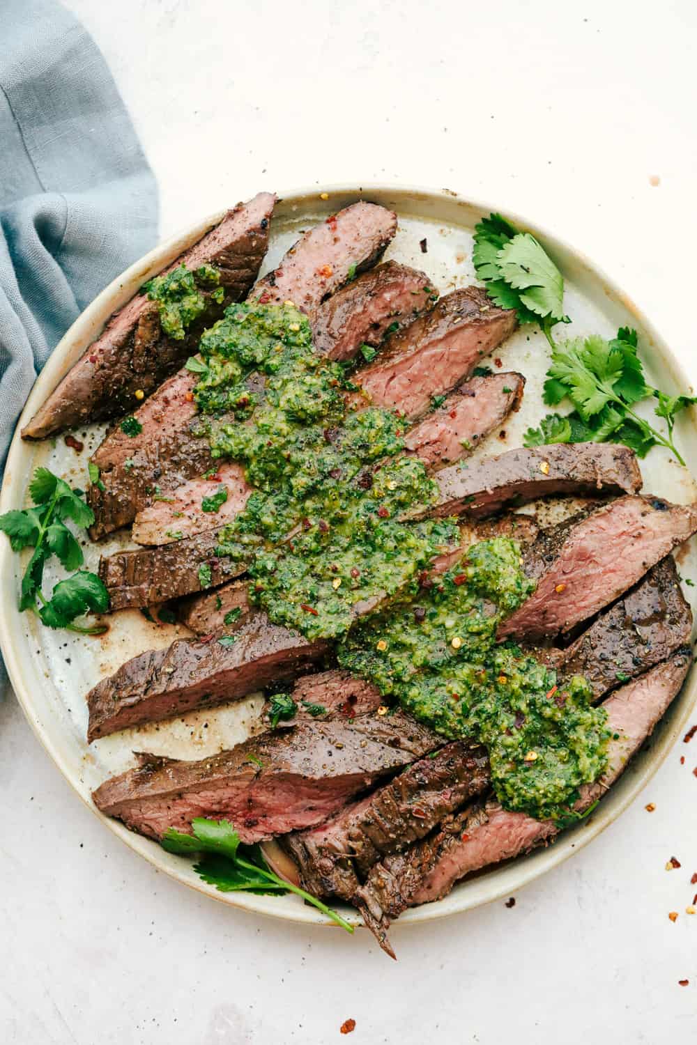 Flank steak sliced against the grain with chimichurri sauce on top on a white plate. 
