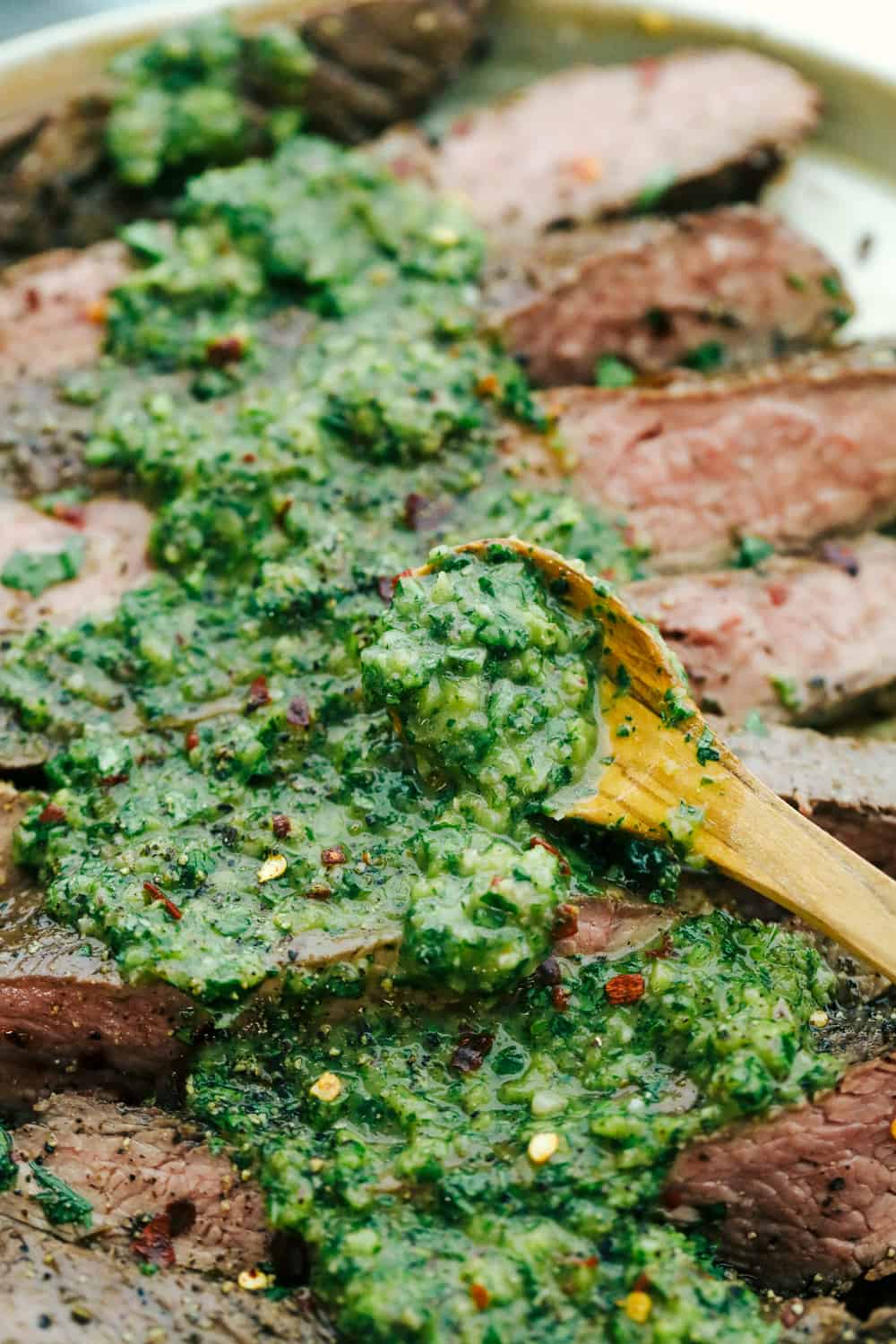 Flank steak sliced up with an up close photo with chimichurri sauce with a wooden spoon spread over top. 