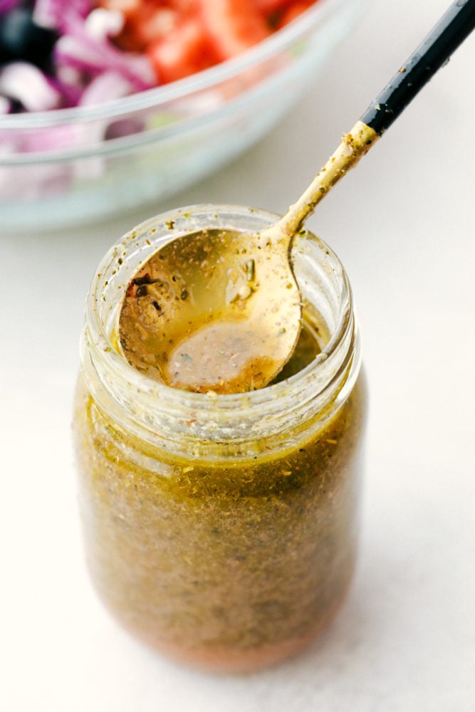 Greek Salad Dressing in a jar with a spoon in it. 