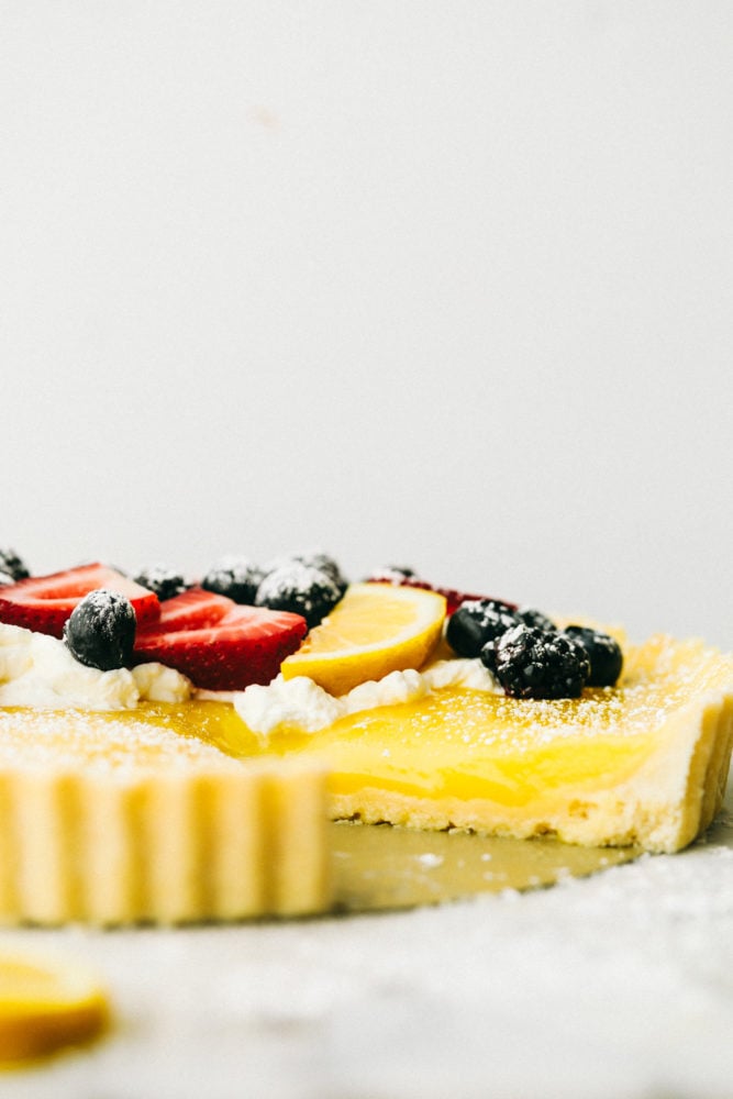 Foto de tarta de limón de un lado del postre con bayas frescas en la parte superior y azúcar en polvo. 