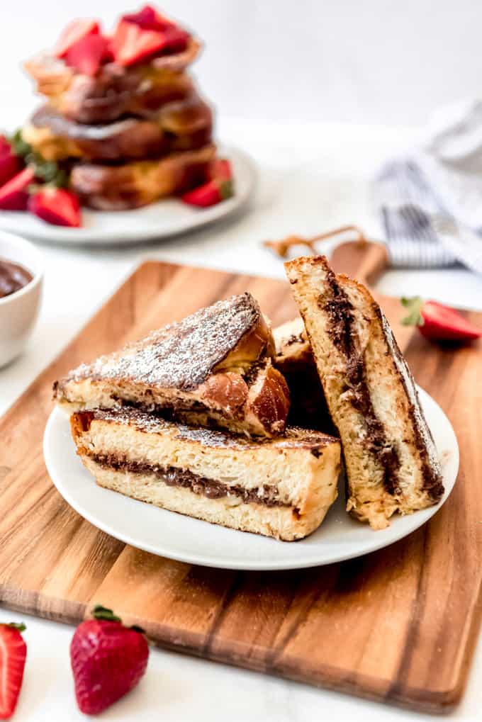 Una imagen de nutella rellenas tostadas francesas en rodajas por la mitad en un plato.