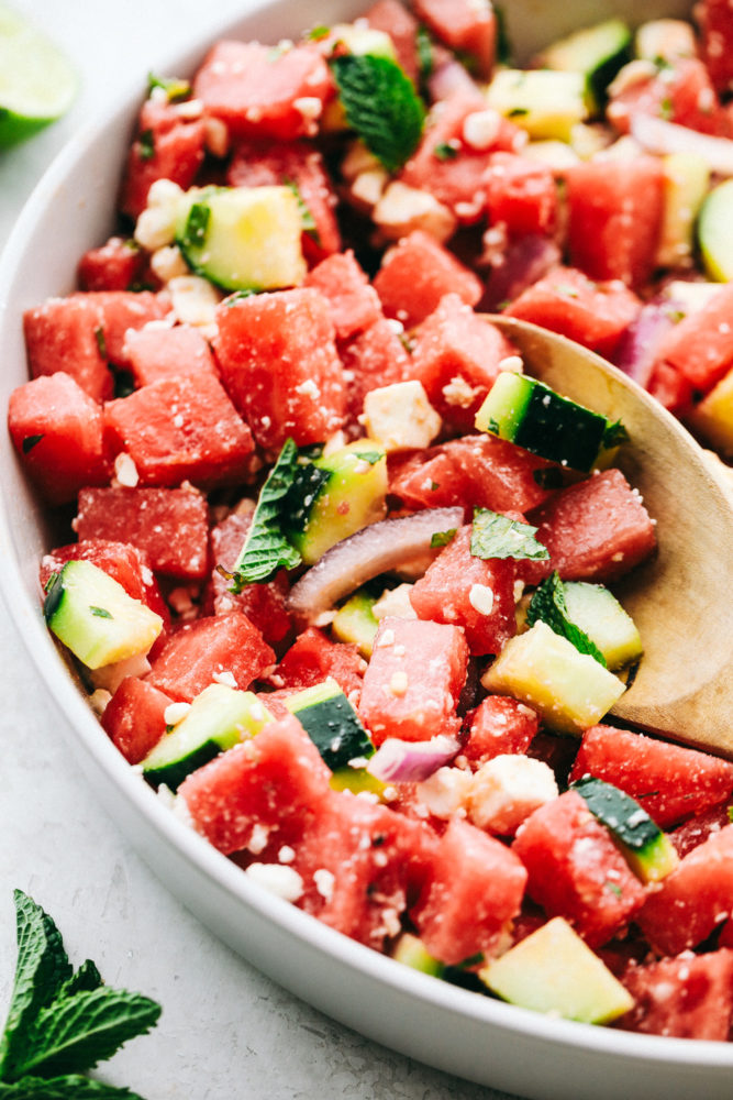 Watermelon salad in a white bowl with a wooden spoon in the salad. 