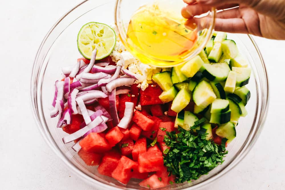 Ingredients of the salad in a glass bowl separated and having the dressing being poured overtop. 