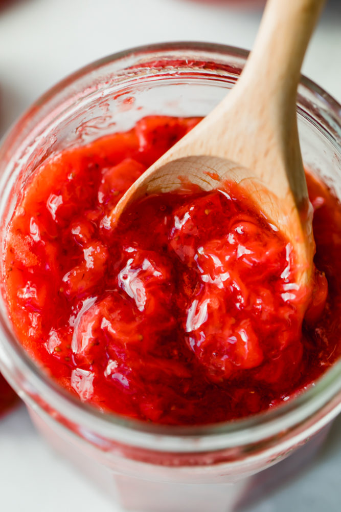 Strawberry jam in a jar with a wooden spoon in it. 
