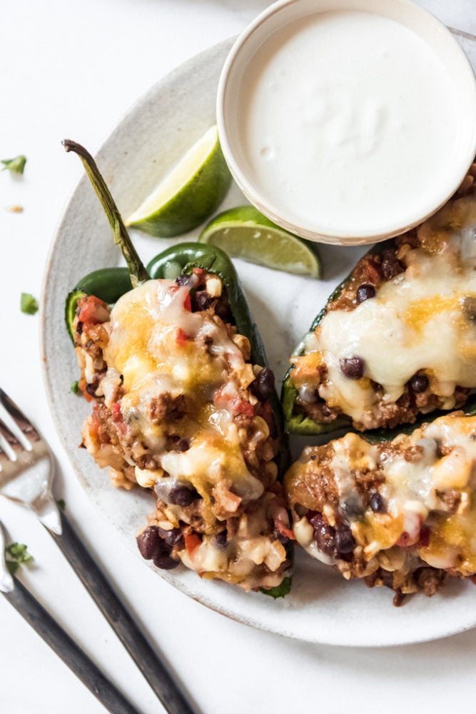 Stuffed poblano peppers on a plate next to a bowl of crema.