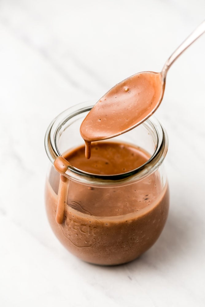 Smooth creamy balsamic dressing in a jar with a spoon dripping dressing back into the jar.