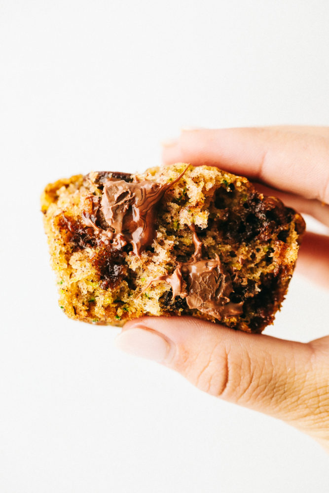 One chocolate chip zucchini muffin being held in the air with a white background. 