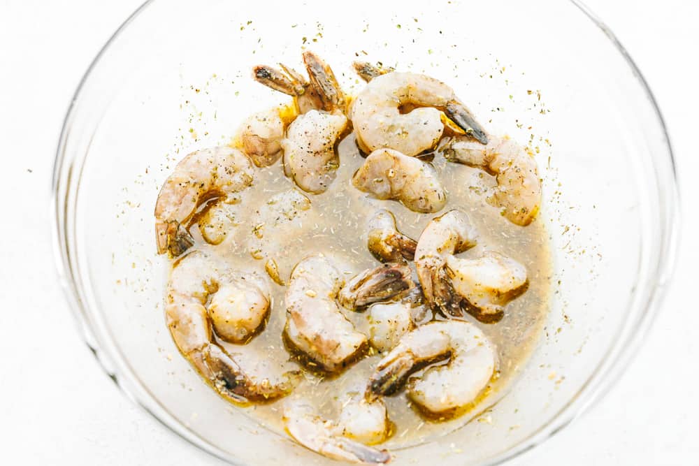 Grilled shrimp marinating in a clear bowl.
