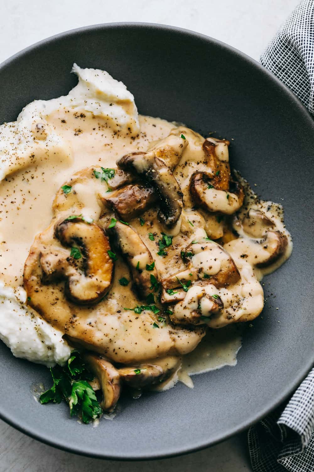 Smothered pork chops plated with mashed potatoes on a black plate.