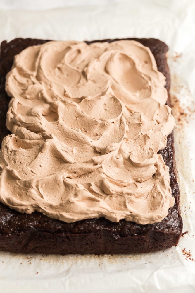 whole chocolate zucchini cake on parchment paper with chocolate whipped cream