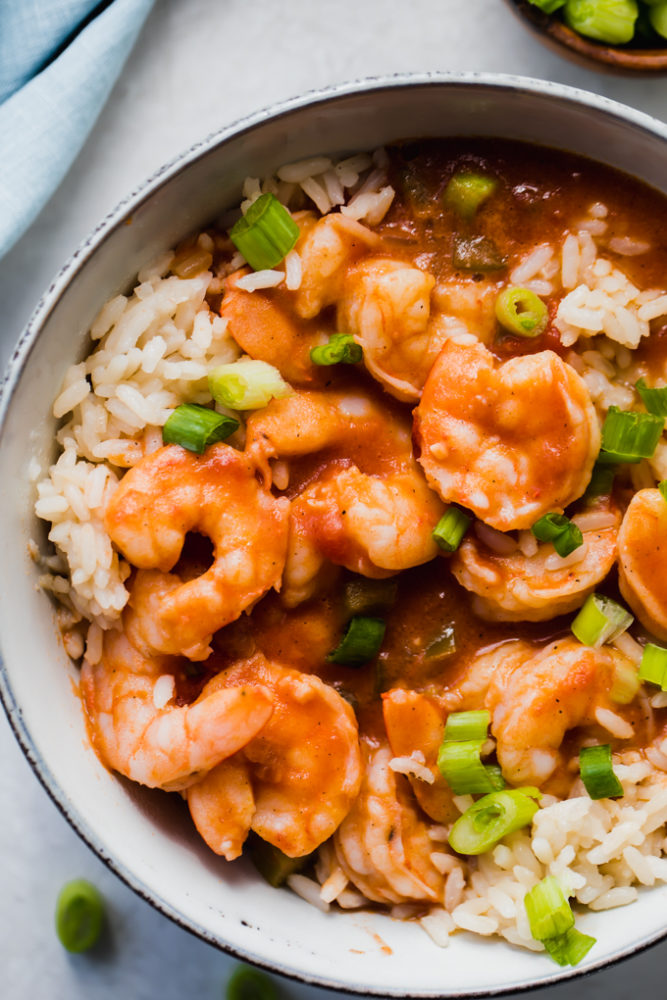 Creole shrimp étouffée over top rice in a bowl topped with scallions. 