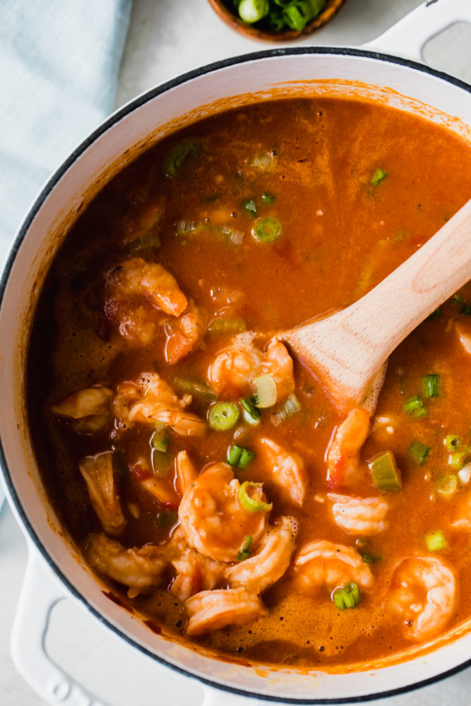 Creole shrimp étouffée in a large pot being stirred with a wooden spoon. 