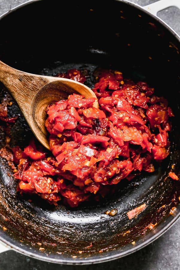 Tomato Jam being stirred with a wooden spoon in a pot. 