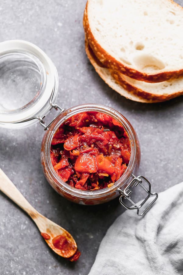 Tomatenmarmelade in einem sauberen Dosenglas mit einem Holzlöffel auf der Seite mit Tomatenmarmelade darauf.