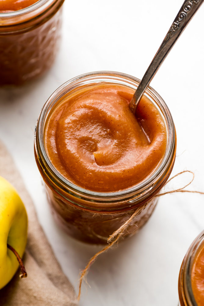A jar of silky smooth Apple Butter with a spoon in it.