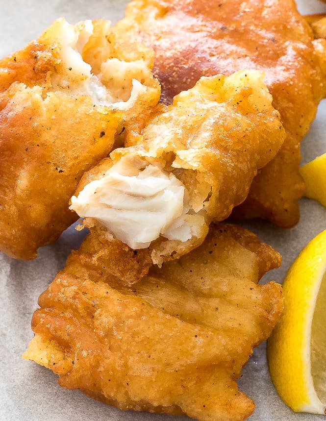 Fried fish on parchment paper with a slice of lemon next to it. 