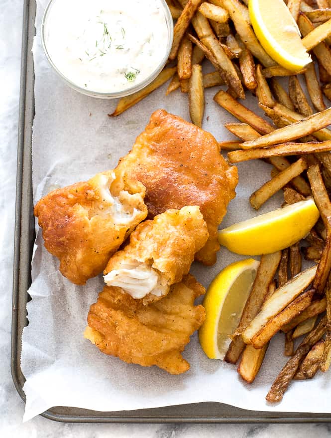 Pescado al lado con papas fritas, ensalada de col y rodajas de limón al lado. 