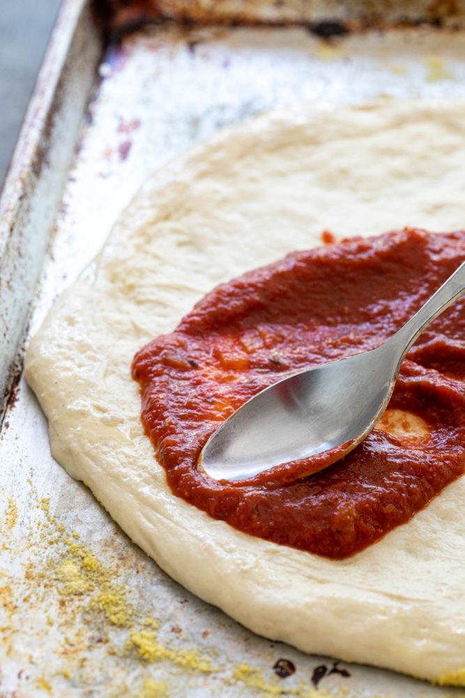 Spoon spreading pizza sauce on dough