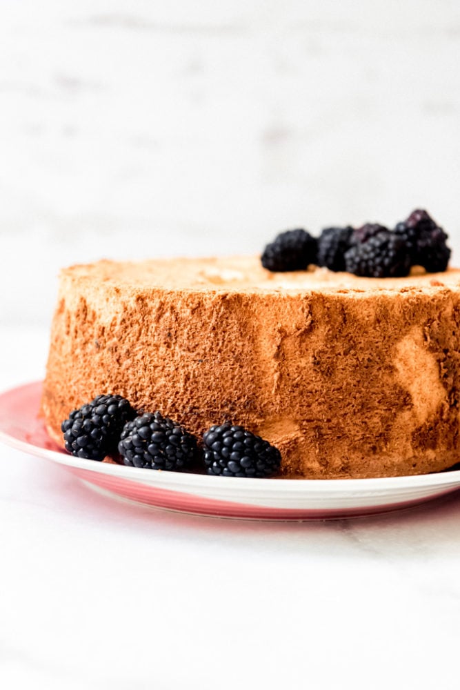 An angel food cake on a plate with blackberries.