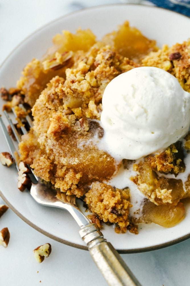 Apple dump cake on a white plate with a fork on the side. Topped with ice cream. 