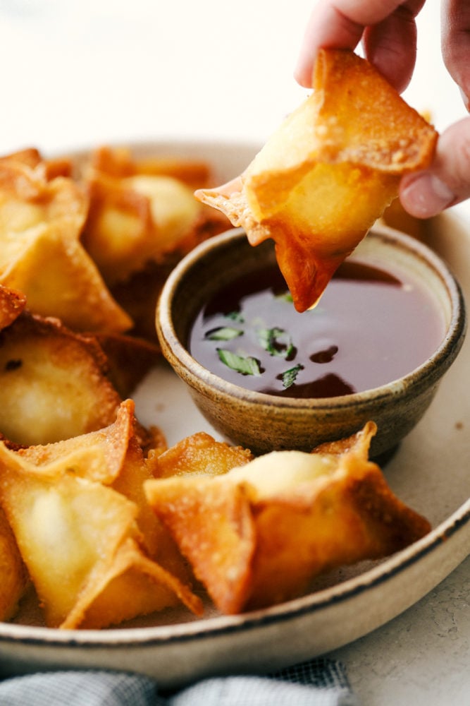 A wonton being dipped in sauce with other cream cheese wontons on the side. 