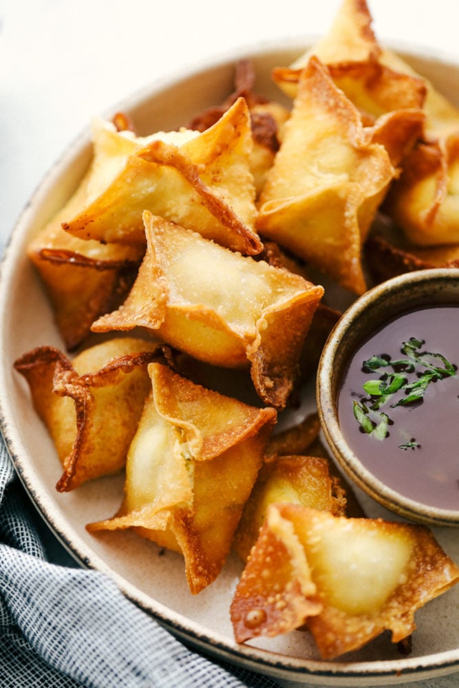 Cream cheese wontons in a creamy bowl with a side of sauce. 