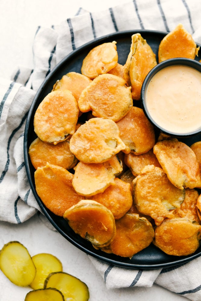 Fried pickles on a black plate with dipping sauce. 