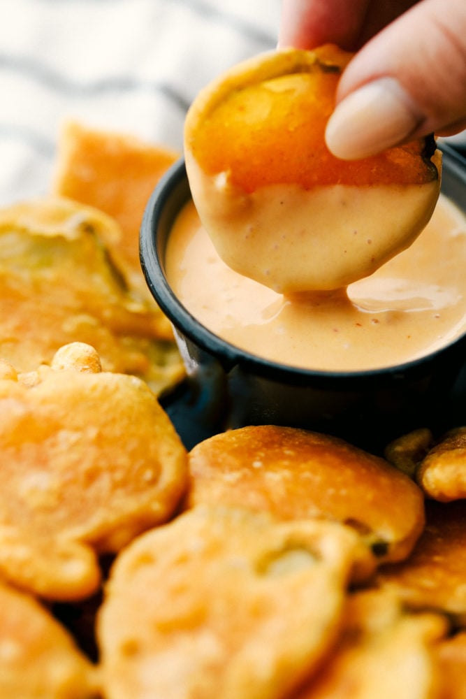 Fried pickle being dipped in a sauce dip with other fried pickles on the side. 