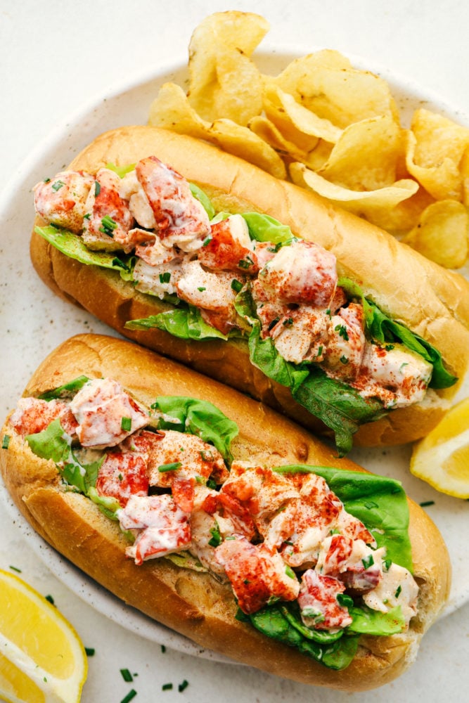 Finished lobster rolls on a white serving plate with chips.