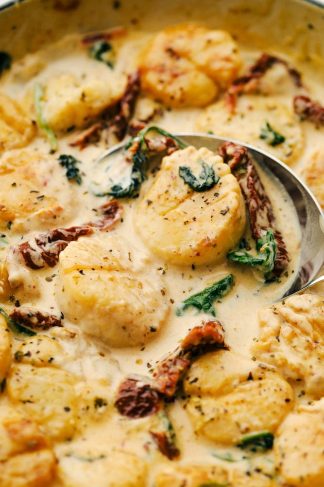 Tuscan garlic scallops in a skillet with a spoon stirring it together. 