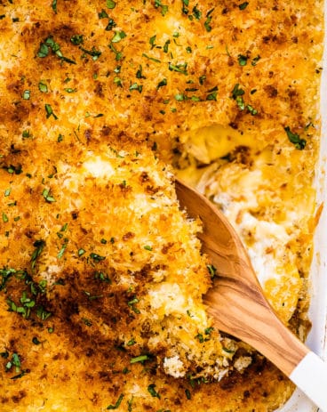 A spoon taking a scoop of chicken divan out of a white casserole dish.