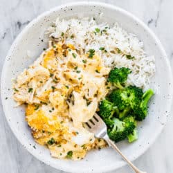 A white bowl with chicken divan with broccoli and rice on the side.