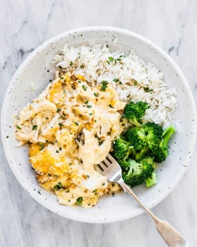 A white bowl with chicken divan with broccoli and rice on the side.