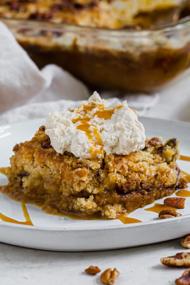 Pumpkin dump cake topped with whipped cream and caramel sauce.