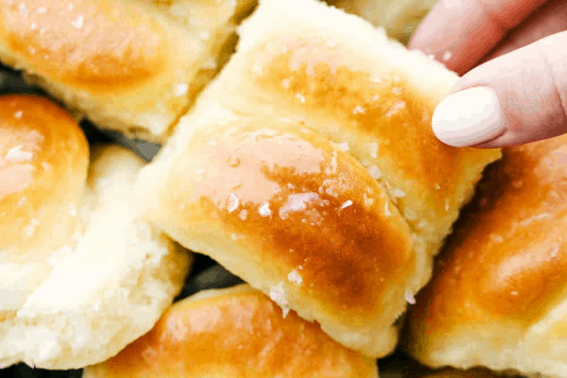 Hand holding homemade rolls sprinkled with rock salt on counter 