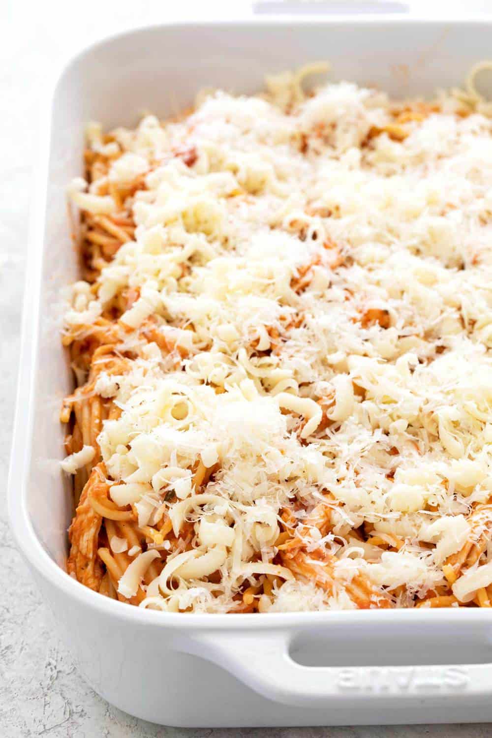 Lots of shredded cheese in a casserole dish with pasta