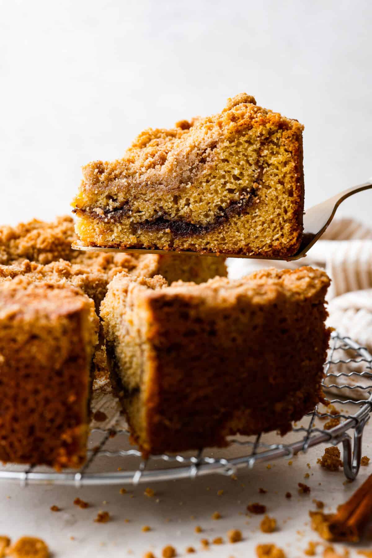 Side shot of a slice of cinnamon coffee cake being lifted off the cooling rack.