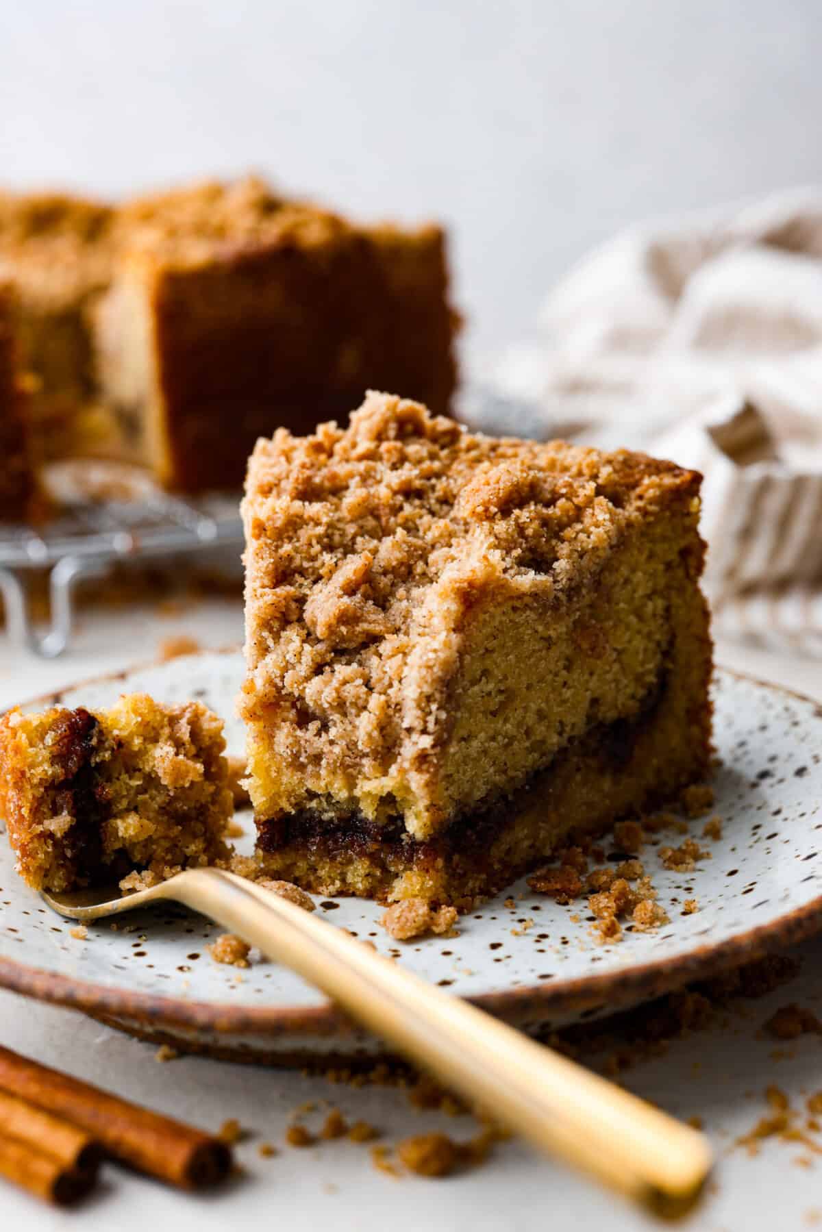 Close up shot of a slice of cinnamon coffee cake on a plate with a gold fork with a bite on it. 