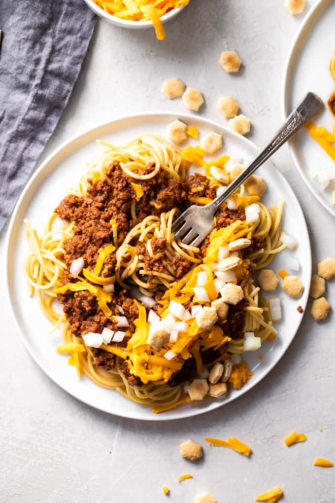 A white plate with Cincinnati chili and noodles wrapped around a fork. 