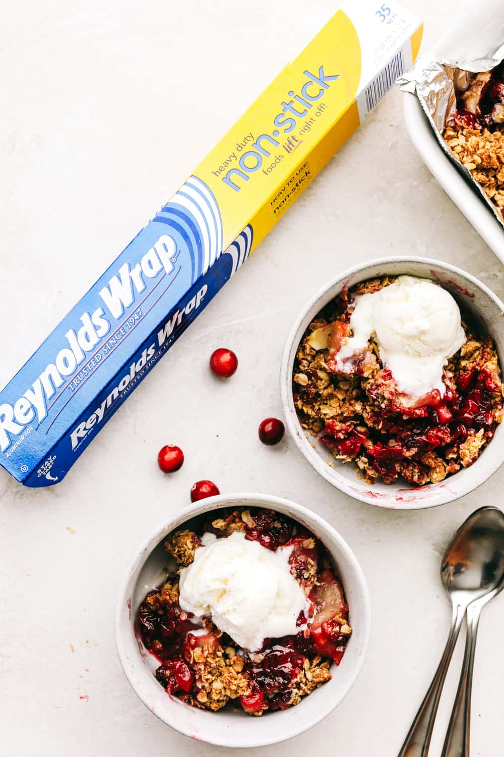 Cranberry apple crisp in two bowls with a scoop of vanilla ice cream over top. 