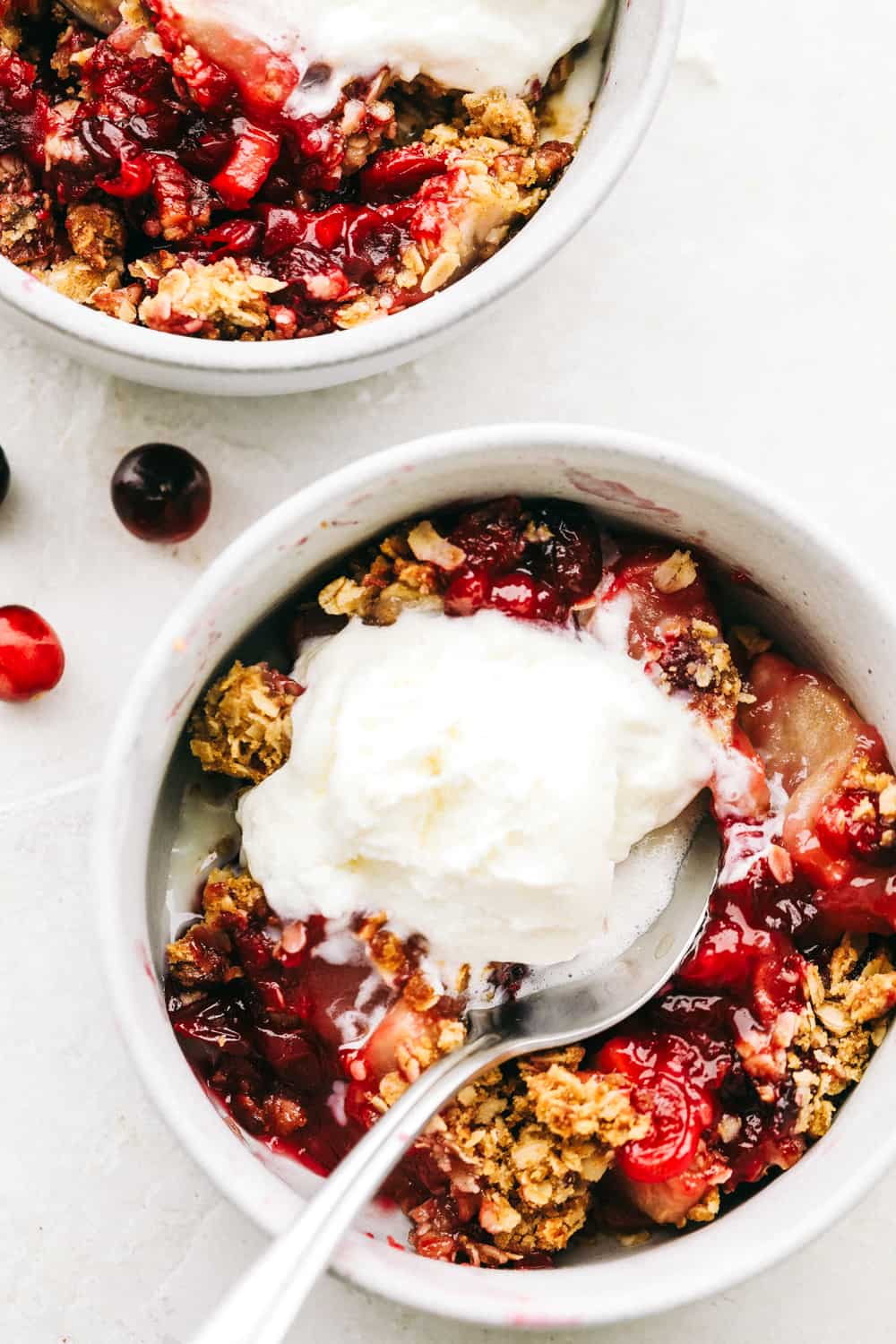 Cranberry apple crisp in two bowls with a scoop of vanilla ice cream overtop. 