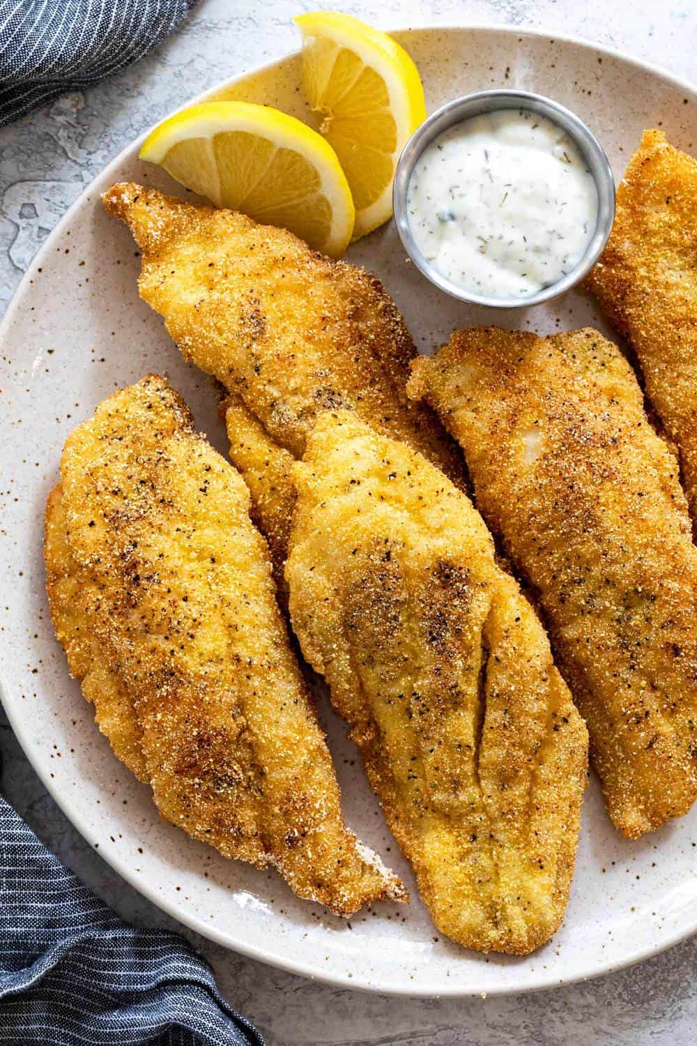 Fried Catfish on a white plate with two lemon slices. 