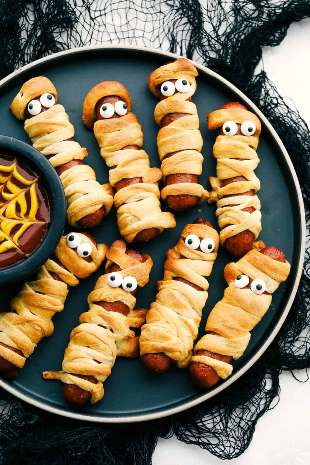 Mummy Hot dogs on a plate with spider webb dip.