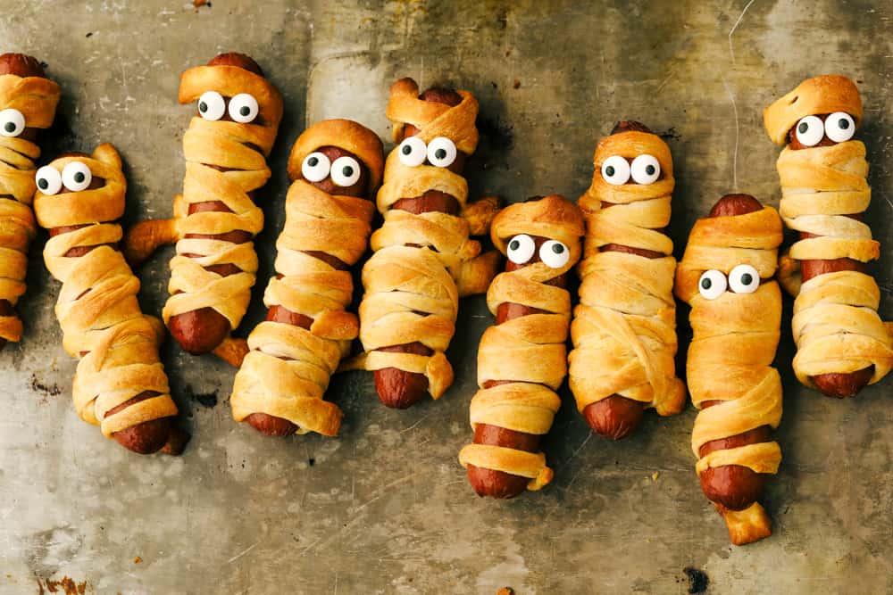 Cooked mummy hot dogs on a pan with eyes.