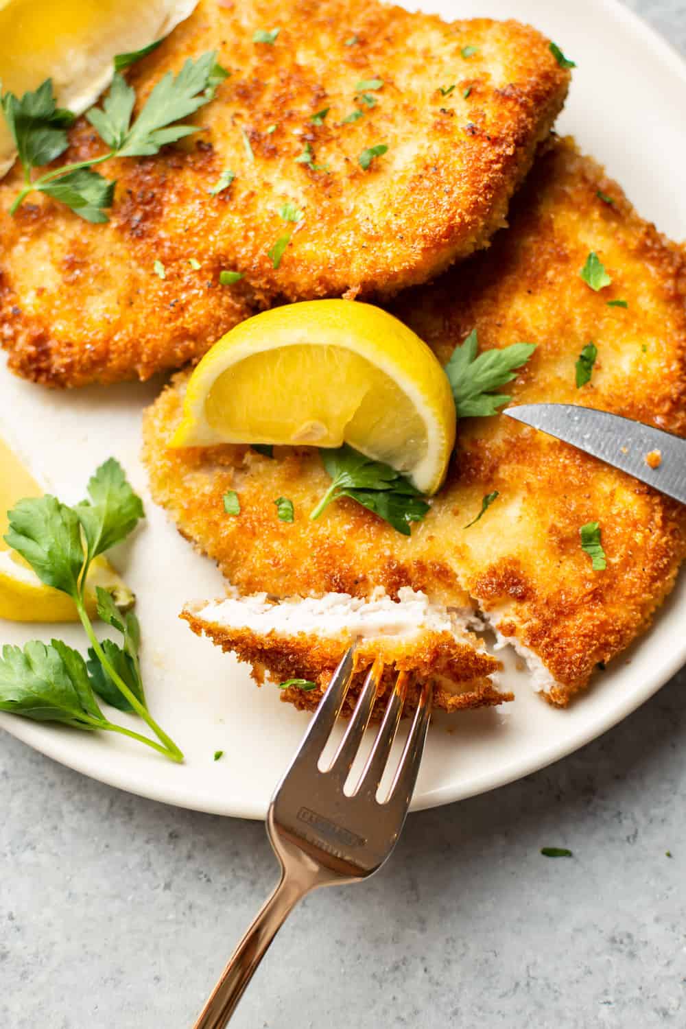 pork schnitzels on a plate with lemon wedges and one schnitzel cut into showing a bite on a fork