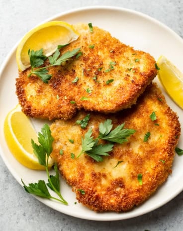 pork schnitzels on a plate with lemon wedges