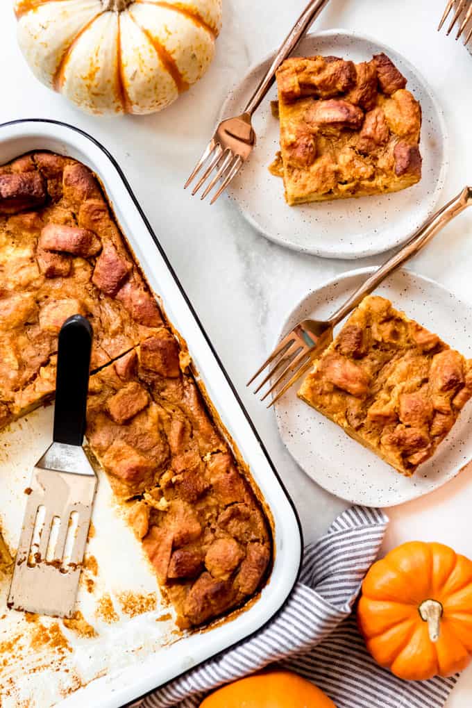 Slices of bread pudding on plates with forks next to small pumpkins.